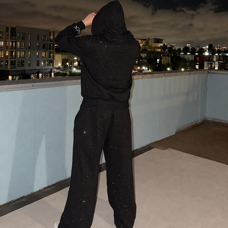 Model wearing black M&N Orgullo rhinestone hoodie on rooftop at night