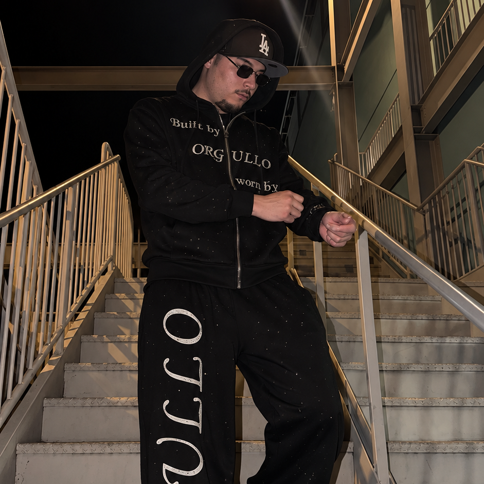 Model wearing black M&N Orgullo rhinestone zip-up hoodie on stairs