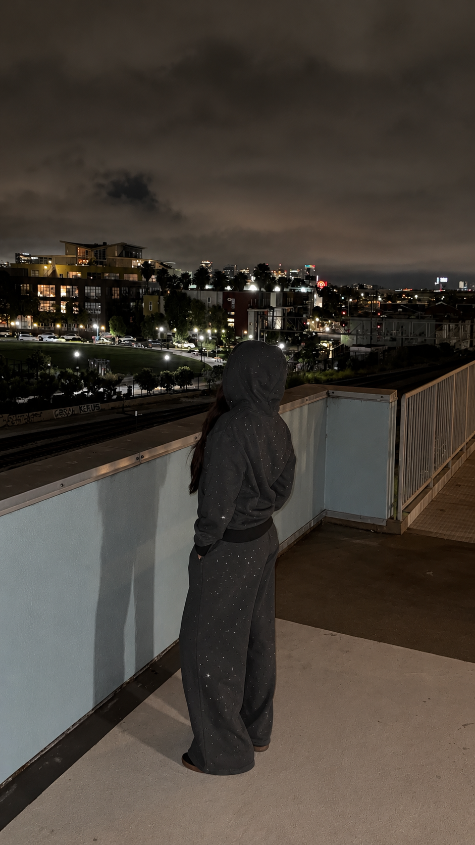 Model wearing dark gray M&N Orgullo rhinestone sweatpants on rooftop at night